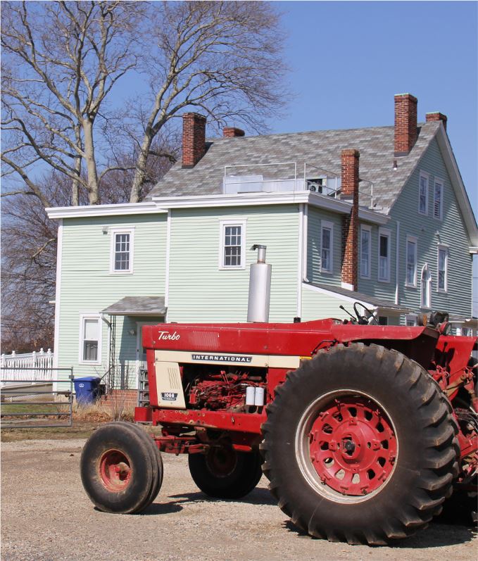 Old cabless red tractor in front of a house