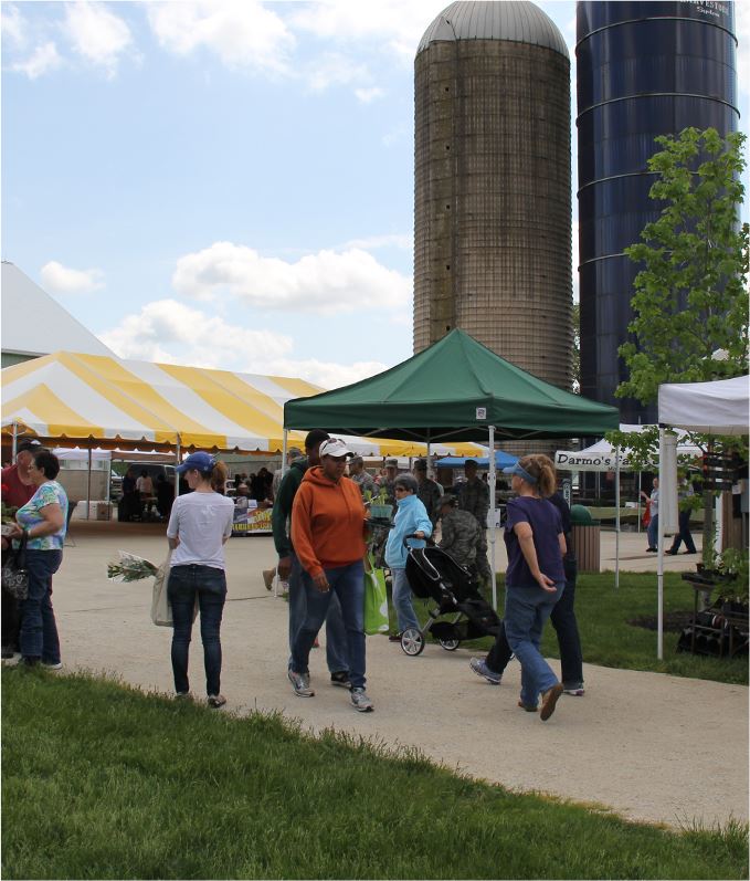 People walk around tents and displays with two silos in the background